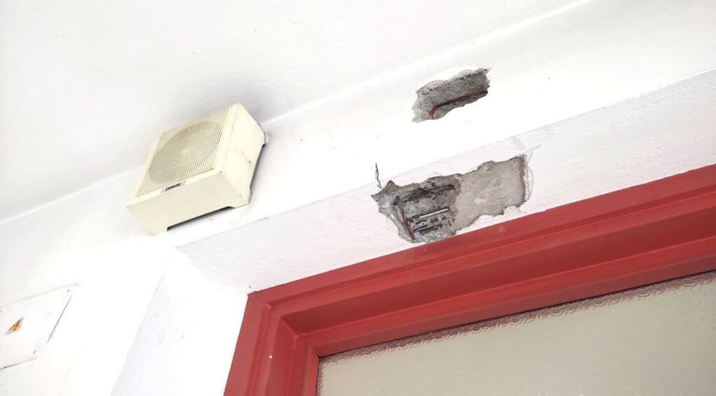 Distacco dell'intonaco sopra un portone dell'autorimessa della caserma dei Vigili del Fuoco in Brianza con armature metalliche in vista, evidenza del degrado del calcestruzzo armato