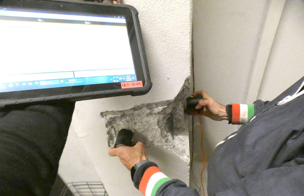 Tecnico che esegue prove ultrasoniche dirette con strumento ULT-12-PC su un pilastro in calcestruzzo armato dell'autorimessa della caserma dei Vigili del Fuoco